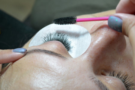 Extension of artificial eyelashes for an adult woman, a master combing eyelashes with brush