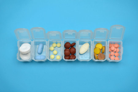 Plastic daily organizer for pills, box with different pills on a blue background with copyspace, top...