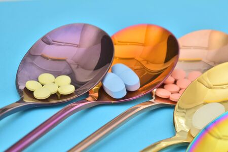 Five different types of pills in five multi colored shine metal spoons on a blue background closeupの写真素材
