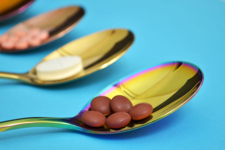 Three different types of pills in three colored shine metal spoons on a blue background