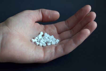 White small square pills lie in the male palm on a black background, side viewの写真素材