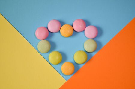 Round colored candies lie in the shape of a heart on three color triangles, yellow, blue and orange, geometric backgroundの写真素材