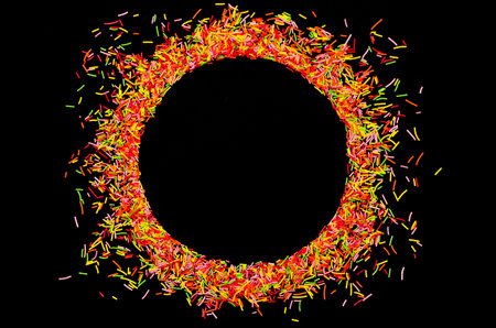 Sugar long baking sprinkles in the shape of a circle frame on black background, concept and...