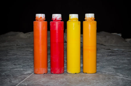 Four long bottles with paints, autumn colors, red, yellow, orange, stand on a dirty floor during...