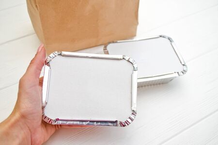Mockup for delivery of fast food, foil plates with a cardboard cover, in woman hand, near a paper bag on a white backgroundの写真素材