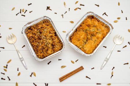 Indian food, fruit pies, subhadra and mithai, in foil plates on a white background, sprinkled with seeds, spices, cinnamon stick, with two forksの写真素材
