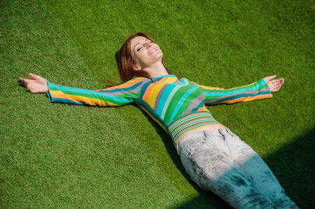 Cute red haired caucasian girl in gray jeans, rainbow blouse, smiling calm and totally happy, lay on...