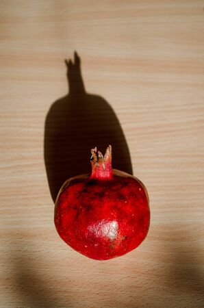 Ripe red fruit pomegranate on a light wooden table under the direct rays of the sun and a hard long shadow, top vertically viewの写真素材