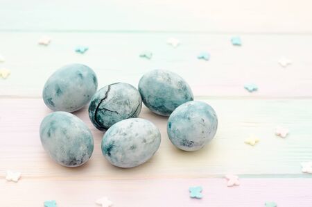 Six blue marble eggs, one of them with a crack, painted in hibiscus tea, lie on a rainbow background with a sprinkle of butterfliesの写真素材
