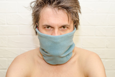 Emotional crazyand tired caucasian man with shaggy hair, on white brick background with a blue scarf...