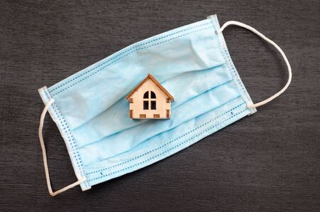 Small wooden house is inside a blue medical mask, on a black background, the concept of the coronavirus epidemic, stay at home or go in a maskの写真素材