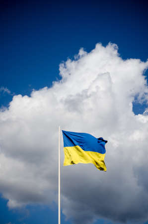 Blue and yellow Ukrainian national flag on a flagpole against a blue sky and white clouds, flag waving in the windの写真素材