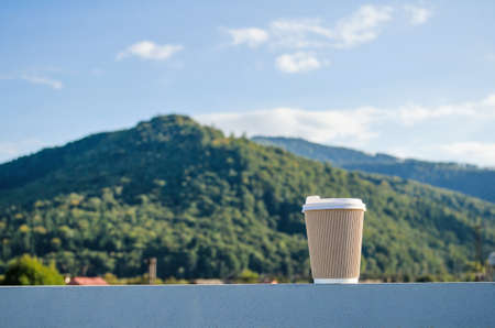 Brown disposable cup of coffee on the background of green carpathian mountains and blue skyの写真素材
