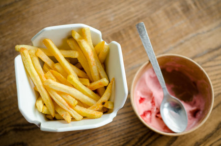 Fries and ice cream with a spoon are served at the restaurant in a in white porcelain and paper boxes on a wooden tableの写真素材