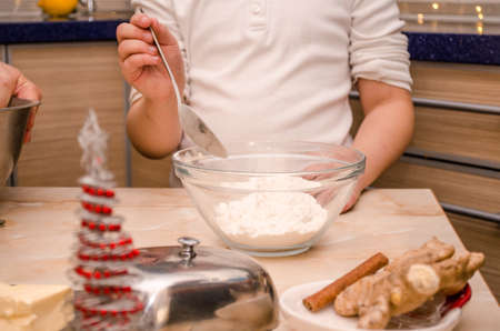 Hands of young girl prepare festive Christmas gingerbread cookies for christmas, she pours flour on the doughの写真素材