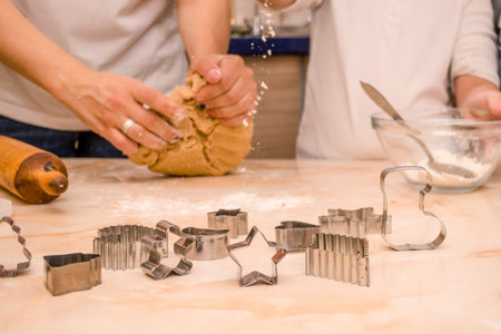 Hands of mother and daughter prepare festive gingerbread cookies for christmas, daughter pours flour...