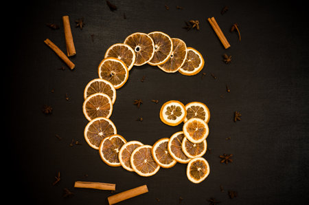 Set for mulled wine on a black background, in form of letter G, scattered dry oranges, cinnamon, cloves, star anise, with copyspaceの写真素材