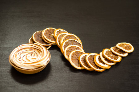 Delicious sweet orange tart with a baked top, black background with slices of dry fruit, as a background for holiday menus and postsの写真素材