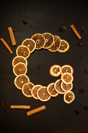 Set for mulled wine on a black background, in form of letter G, scattered dry oranges, cinnamon, cloves, star anise, with copyspaceの写真素材