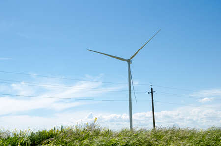 Wind turbine and power line support in yellow rapeseed field, background of blue sky and beautiful white clouds, source of alternative energyの写真素材