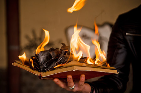 Paper book burns to ashes on concrete tiles, manuscript burns, open book with burning fire in man handの写真素材