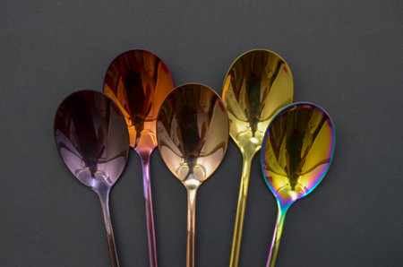 Multicolored table spoons on a plain black background, picture for an article about tableware or cutlery, with a copyspaceの写真素材