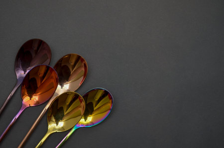 Multicolored table spoons on a plain black background, picture for an article about tableware or cutlery, with a copyspaceの写真素材