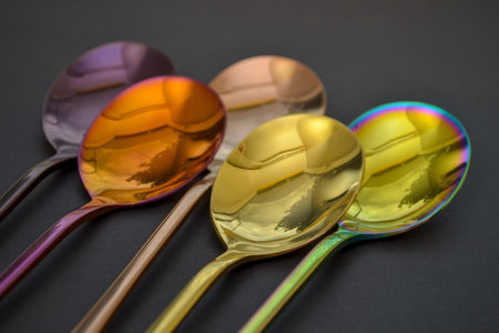 Multicolored table spoons on a plain black background, picture for an article about tableware or cutlery, with a copyspaceの写真素材
