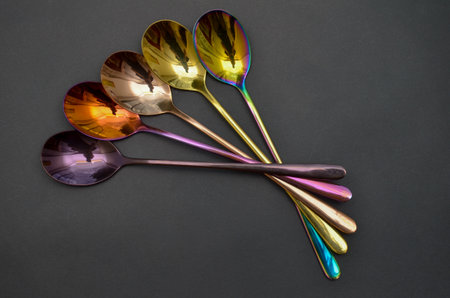 Multicolored table spoons on a plain black background, picture for an article about tableware or cutlery, with a copyspaceの写真素材
