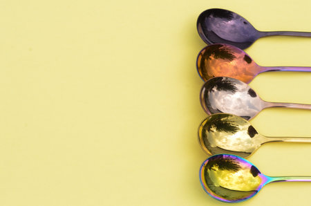 Multicolored table spoons on a plain yellow background, picture for an article about tableware or cutlery, with a copyspaceの写真素材