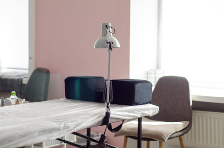 Workplace of the master of eyelash extension or lamination of eyelashes and eyebrows. A bright office with a large window behind and a lamp, a lying place, a chair and a couchの写真素材