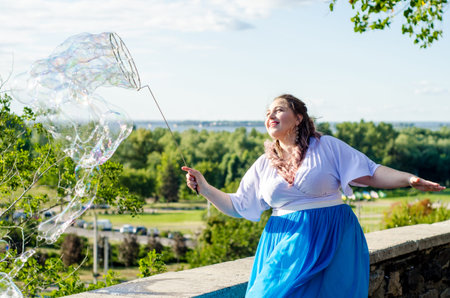 Street performer, beautiful young woman in blue skirt and white blouse, with soap bubbles shows soap...