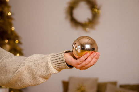 Large mirror Christmas tree decoration in the form of a ball, in the hand of a young woman in the background of a bright room with a Christmas wreathの写真素材