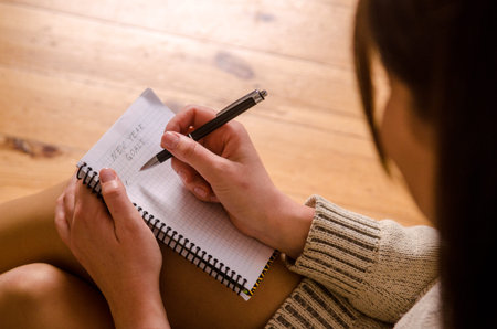 Young beautiful woman in a sweater, sitting in the Christmas room, writes in a notebook with a black...