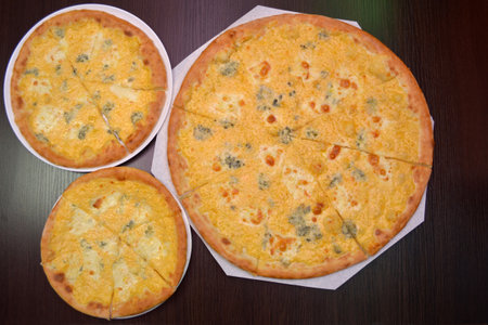Three delicious fresh round four cheeses pizzas on a black table, surface, on a white plates, three different sizes for serving in a pizzeriaの写真素材