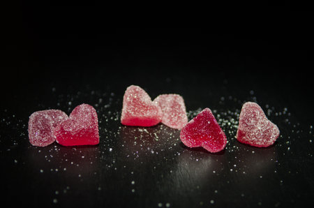 Six red sugar marmalade candies in the shape of heart on a black background, lit from the side, with copyspaceの写真素材