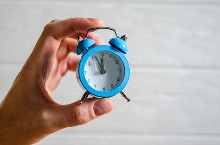 Classic arrow blue alarm clock on a man hand on a white background, concept of the passage of timeの写真素材