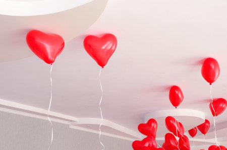 Red heart shaped inflatable helium balloons hang from the ceiling during a birthday partyの写真素材