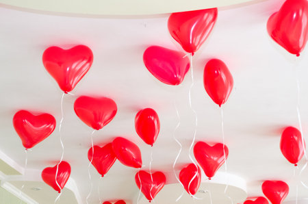 Red heart shaped inflatable helium balloons hang from the ceiling during a birthday partyの写真素材