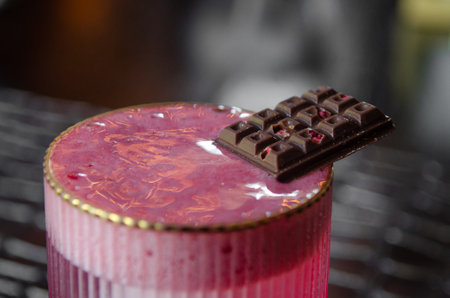 Red grapefruit cocktail with foam, ice and a piece of chocolate on a black table in a restaurantの写真素材