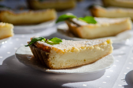 Triangular pieces of cheesecake with mint on white plates with forks, under the sun rays, catering at the eventの写真素材