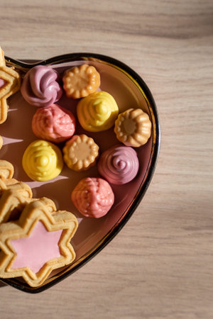 Pink star shaped cookies, multicolored gelatin candies in a heart shaped saucer on a beige wooden...