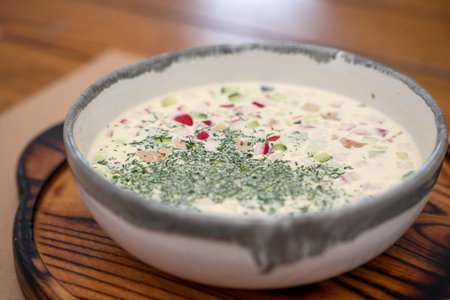 Traditional eastern European cold soup okroshka served on a wooden board. Fresh summer dish made with cucumbers, radishes, herbs and kefir. Rustic homemade style food photography.の写真素材