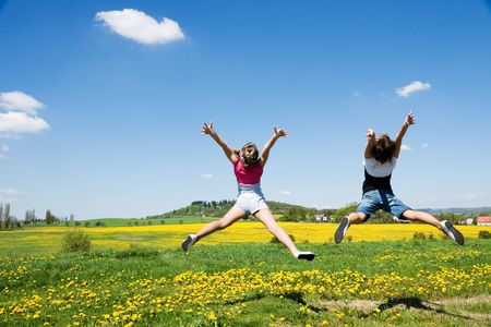 happy girls jump in field under blue sky and cloudsの写真素材