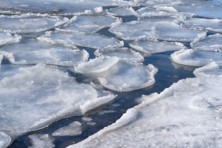 Spring background with melting ice on the surface of a frozen bay. Snowy shore of a frozen lake.