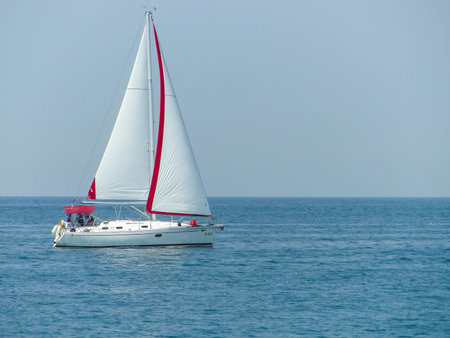 A white boat with a white sail floats on a calm blue sea.の写真素材