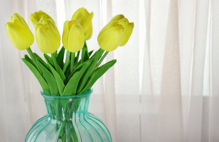 Bouquet of yellow roses in a transparent blue vase in the home interiorの写真素材