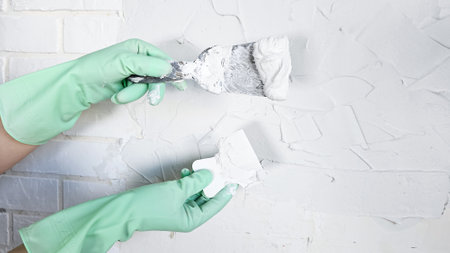 The hand of a worker holding a spatula for applying putty to the wallsの写真素材