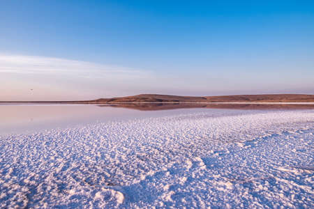 beautiful sunset on a pink salt lake with crystals from salt and brown mountains on the horizon. the sky is reflected in the waterの写真素材