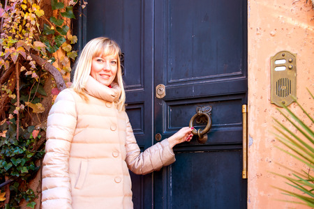 Young woman standing at the door of an old house on a sunny autumn day.の写真素材
